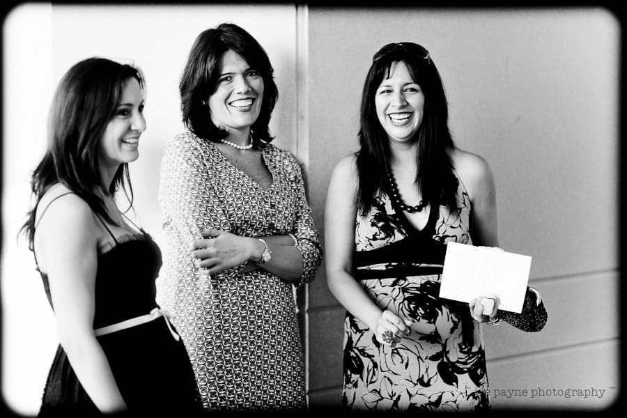 justin and meredith get hitched Three women are standing and smiling. The woman in the middle is wearing a patterned dress, and the woman on the right is holding papers and wearing a floral dress. The image is in black and white.