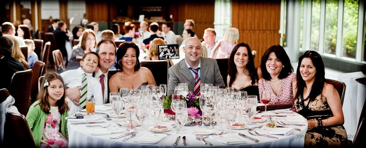 justin and meredith get hitched A group of people posing for a photo around a round table at a formal event. The table is set with glassware, plates, and a floral centerpiece. People are smiling and dressed in semi-formal attire.