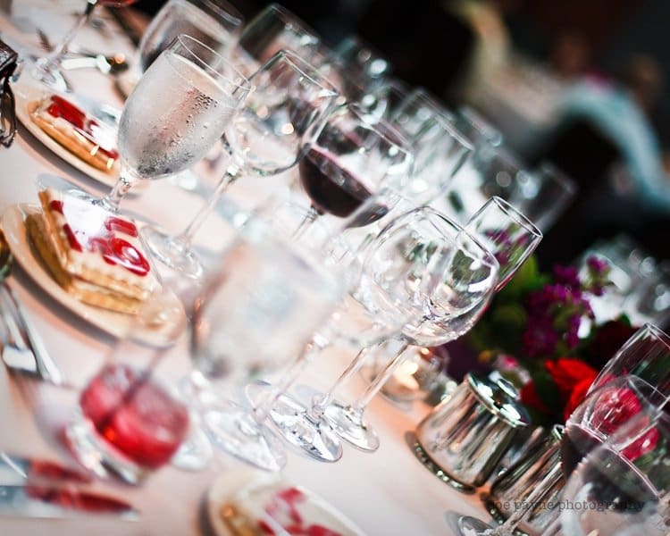 justin and meredith get hitched A table set with an array of wine glasses and water goblets, featuring plates with desserts topped with strawberry slices. The table is elegantly arranged for a formal event, with dim lighting and floral decorations.