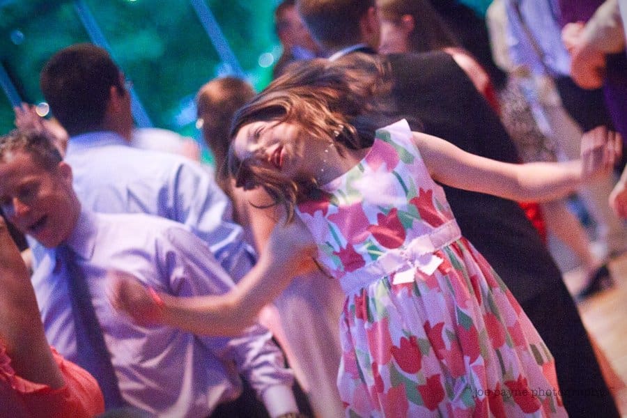justin and meredith get hitched A young girl in a floral dress joyfully dances with her hair swirling, surrounded by a crowd of people at a lively event.