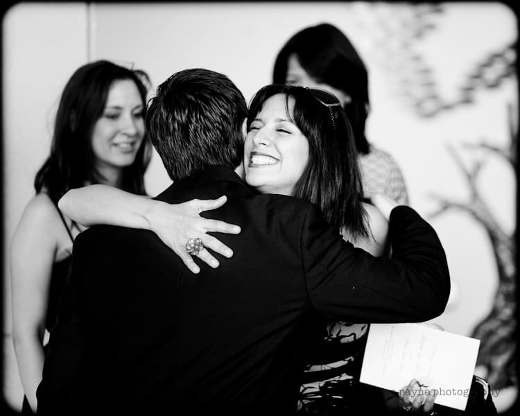 justin and meredith get hitched A black and white photo showing a woman smiling broadly as she hugs a man. Another woman stands in the background with a soft smile. The scene appears joyful and celebratory.