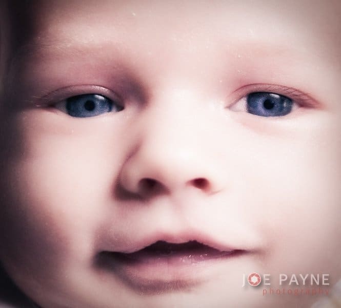 Close-up of a babys face with blue eyes, slightly open mouth, and a soft focus. The image is by Joe Payne Photography, as noted in the lower right corner.