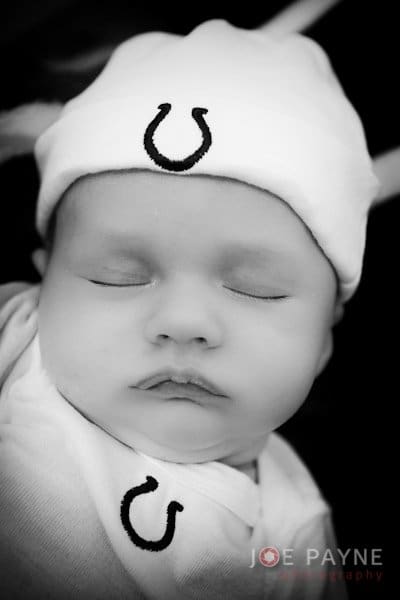 A black and white photo of a baby sleeping peacefully. The baby is wearing a hat and shirt with a horseshoe symbol. The name Joe Payne Photography is visible at the bottom.