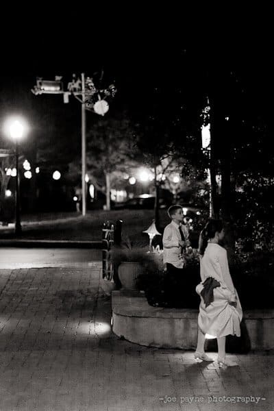 A black and white photo of two people walking on a dimly lit path at night. Trees and streetlights are visible in the background, creating a serene atmosphere. The image is stamped with joe payne photography.