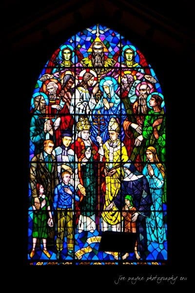 raleigh wedding photographer - jenna and ryan A stained glass window depicting a religious scene with various figures, including a central figure in a yellow robe holding a staff, surrounded by other figures in colorful attire. The background features vibrant, multi-colored geometric patterns.