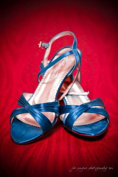 raleigh wedding photographer - jenna and ryan A pair of elegant blue strappy high heels placed on a vibrant red background. The shoes feature a crisscross design at the front and an adjustable ankle strap.