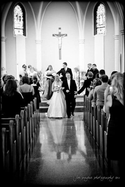 raleigh wedding photographer - jenna and ryan A bride and groom walk down the aisle of a church, celebrating their wedding. The wedding party stands on the altar in the background, and guests watch from the pews.