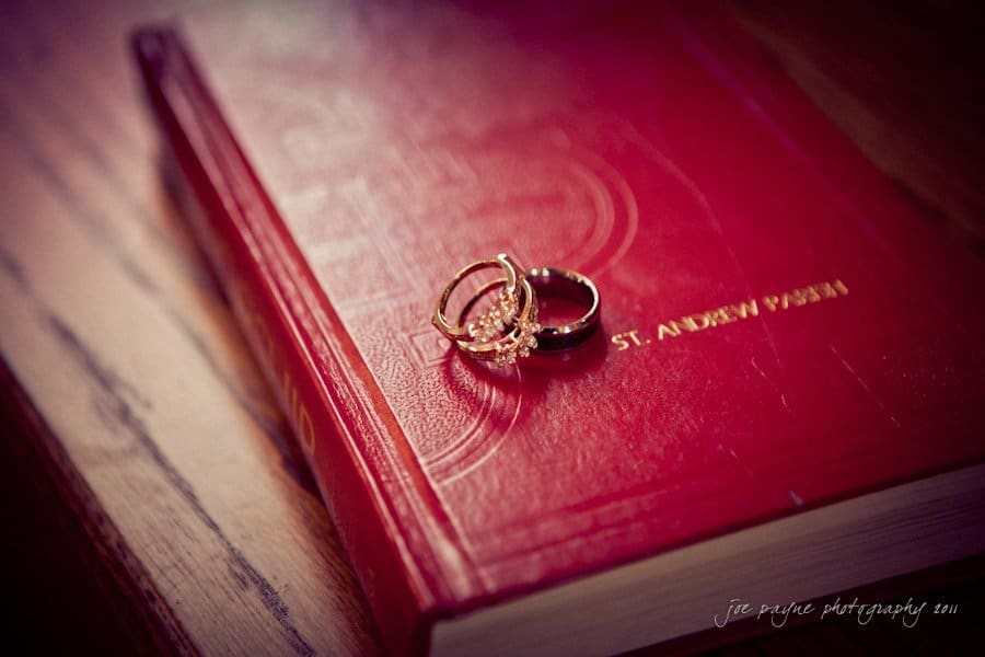 raleigh wedding photographer - jenna and ryan Two rings rest atop a closed red book titled St. Andrew Parish, placed on a wooden surface. The lighting highlights the books embossed details and the rings delicate designs.