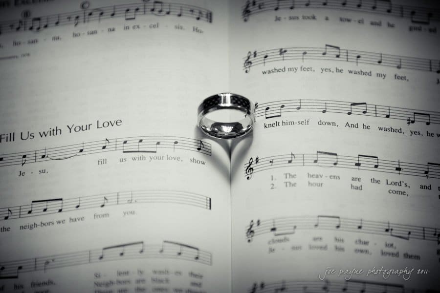 raleigh wedding photographer - jenna and ryan A black-and-white image of an open sheet of music with a ring placed in the center. The ring casts a shadow shaped like a heart on the pages. Sheet music includes lyrics and musical notes. Photographed by jim payne photography.