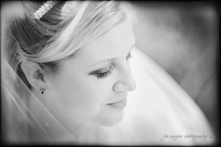 raleigh wedding photographer - jenna and ryan Black and white close-up of a bride with eyes closed, smiling softly. She wears a veil and a headband with pearls. The image has a soft focus, creating a serene and dreamy atmosphere.