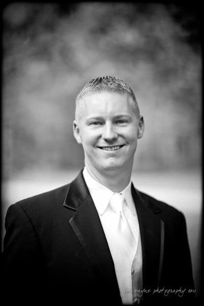 raleigh wedding photographer - jenna and ryan A black and white portrait of a man wearing a tuxedo with a white tie. He is smiling and standing against a blurred background. The photo is signed Joe Payne Photography 2011 in the lower right corner.