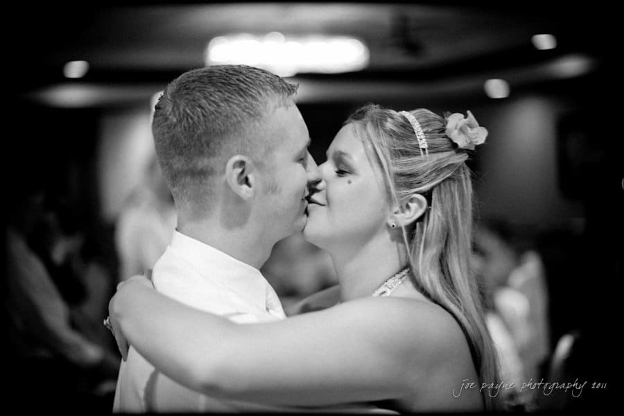 raleigh wedding photographer - jenna and ryan A couple shares a tender moment, dancing closely at an event. The man is wearing a light-colored shirt, and the woman has a flower in her hair and is dressed elegantly. The background is softly blurred, creating a romantic atmosphere.