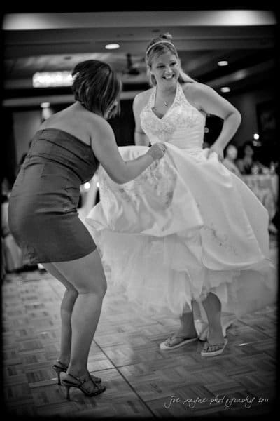 raleigh wedding photographer - jenna and ryan A bride in a white gown smiles while dancing with a woman in a short dress. They are on a dance floor, surrounded by tables and dim lighting, suggesting a wedding reception atmosphere.