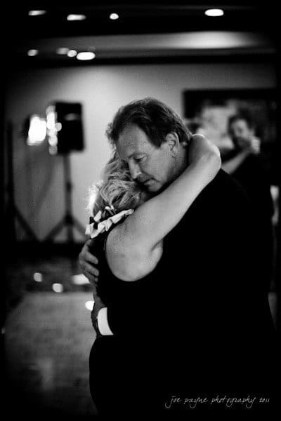 raleigh wedding photographer - jenna and ryan A couple shares an intimate dance in a dimly lit room. They embrace closely, with soft lighting creating a tender atmosphere. The background is blurred, highlighting their connection.
