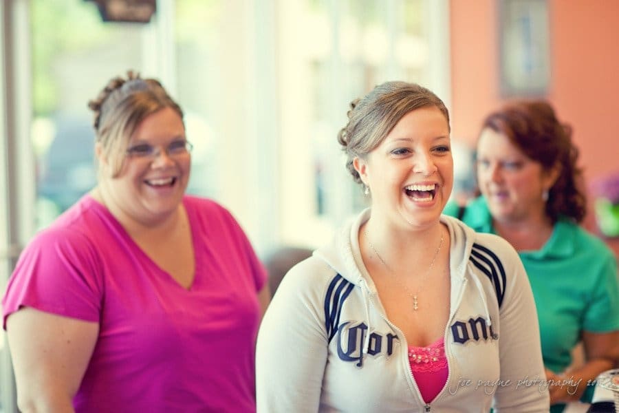 raleigh wedding photographer - jenna and ryan Three women are smiling and laughing in a brightly lit room. One is wearing a pink shirt, another a light grey hoodie, and the third a turquoise top. They appear to be enjoying a candid moment together.