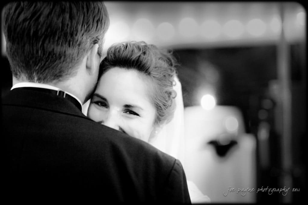 raleigh wedding photographer - image of the week: no. 3 A black and white photo of a bride smiling while embracing someone in a suit, with soft-focus lights in the background.