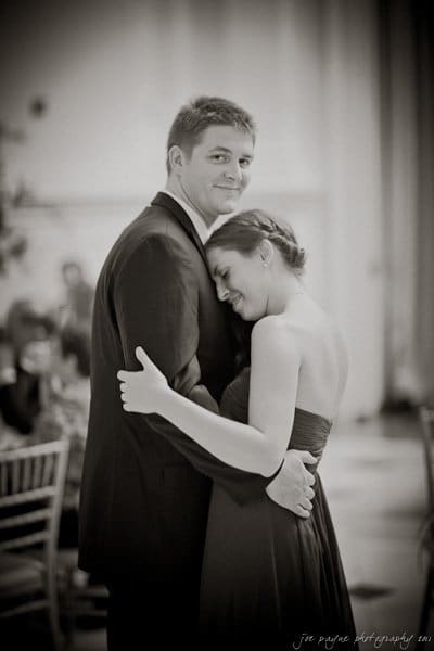 A sepia-toned image of a couple dancing. The man is wearing a suit, and the woman is in a strapless dress, resting her head on his shoulder with her eyes closed. They are embracing each other in a softly lit room.