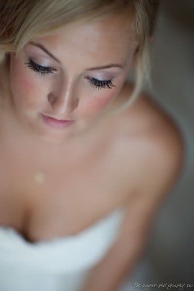 A woman with blonde hair is looking down with closed eyes, wearing a strapless white dress. The photo has soft lighting, creating a gentle and serene atmosphere.