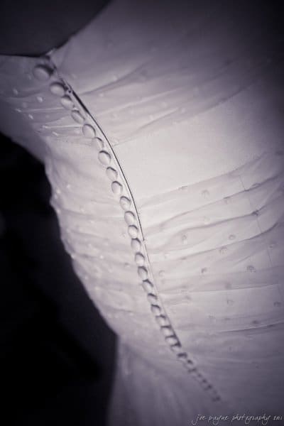 carolina inn weddings | allison and matthew Close-up of a textured white wedding dress featuring a row of small buttons running from top to bottom. The fabric is gathered and pleated, giving it an elegant and delicate appearance.