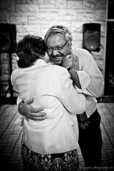 A joyful moment in black and white: a man and woman embrace while dancing, both smiling and laughing. The scene captures a sense of happiness and celebration.