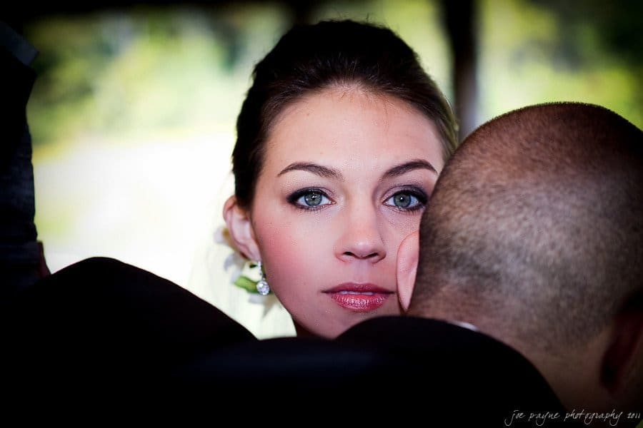 A woman with bright eyes looks at the camera over a mans shoulder. She is wearing delicate earrings, and her hair is elegantly styled. The background is softly blurred, creating a focused portrait.