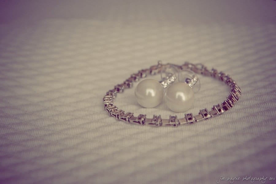 A pearl bracelet and a pair of pearl earrings with silver accents are elegantly arranged on a textured white surface.