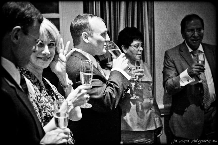 A group of people dressed formally raise their glasses for a toast in a dimly lit room. They are holding champagne flutes and appear to be at a celebratory event.