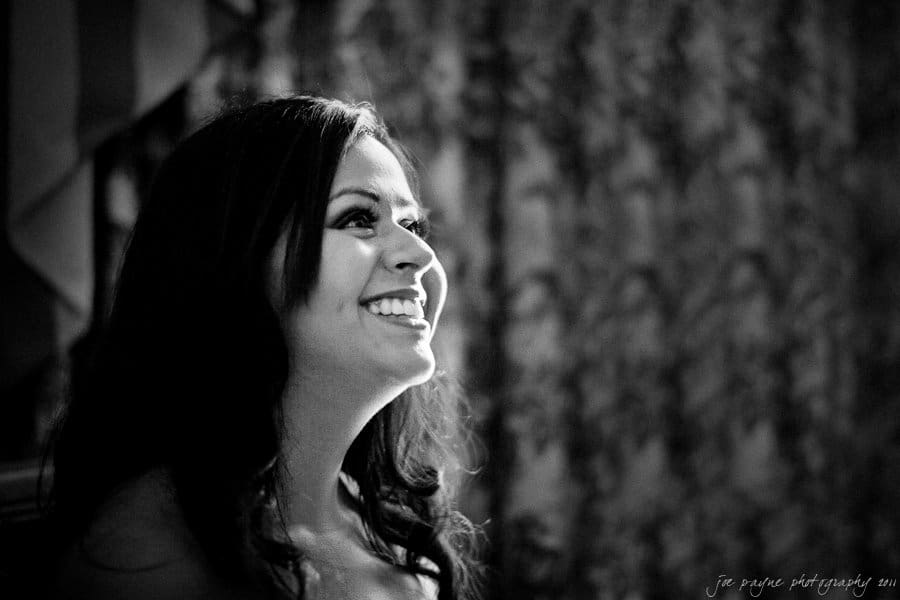 A woman smiling joyfully in a black and white portrait. The background is softly blurred, highlighting her expression.