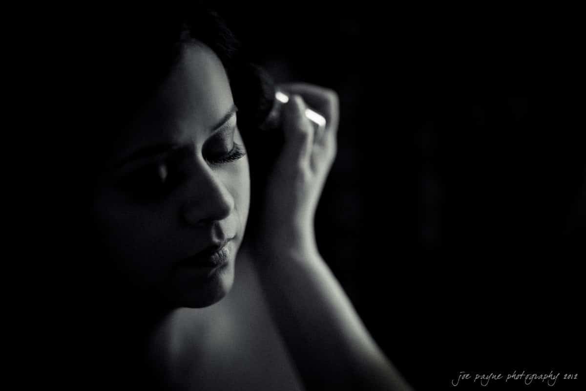 A black and white close-up of a person in low light, with their face partially illuminated. They have closed eyes and are gently touching their hair, conveying a serene and introspective mood.