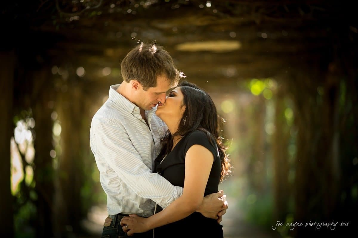 unc chapel hill engagement session ~ thelsa and phil A couple is embracing and about to kiss under a canopy of greenery. Sunlight filters through the leaves, creating a romantic and intimate atmosphere. Both people appear content and affectionate.