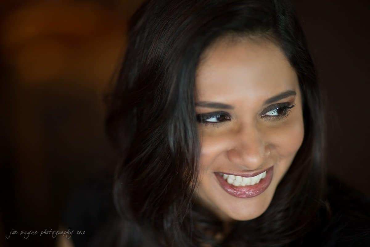 unc chapel hill engagement session ~ thelsa and phil A person with long dark hair is smiling broadly, looking slightly to the side. The background is blurred, emphasizing their face and expression.