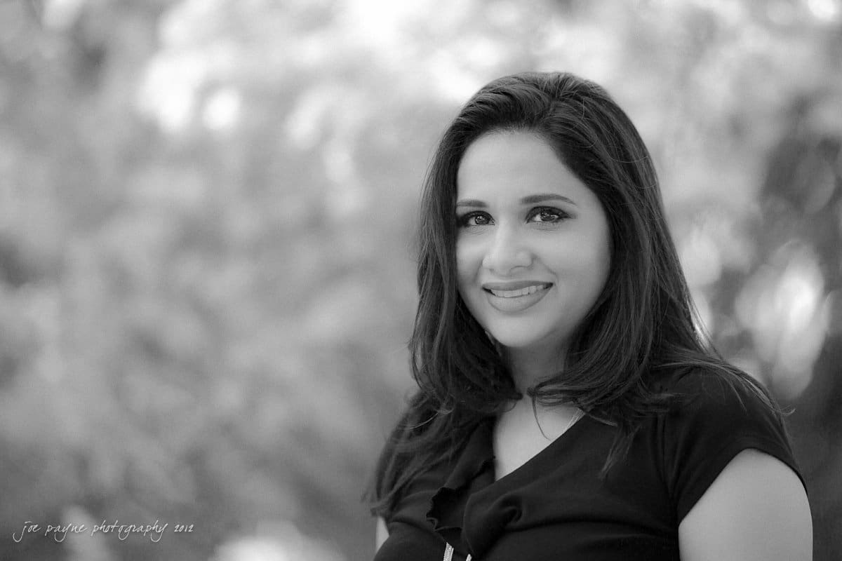 unc chapel hill engagement session ~ thelsa and phil Black and white portrait of a woman smiling at the camera. She has long hair and wears a dark top. The background is softly blurred, creating a gentle and warm atmosphere.