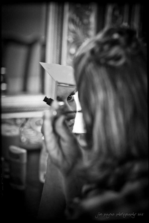lake lure north carolina wedding photography ~ shannon and paul A person applies makeup using a handheld mirror. The reflection shows their face partially visible, concentrating on the task. The black and white image is blurred, creating a soft, intimate atmosphere.
