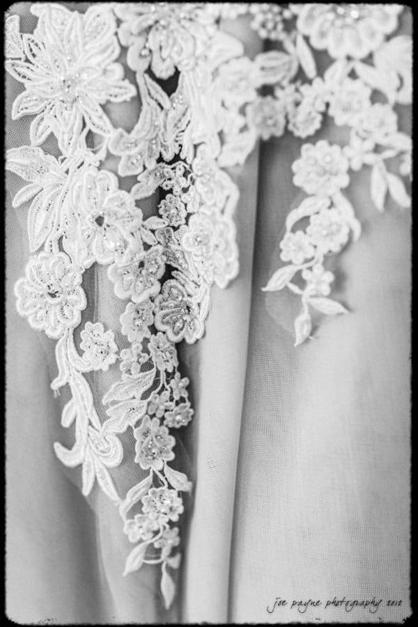 lake lure north carolina wedding photography ~ shannon and paul Close-up of a delicate, white lace fabric with intricate floral embroidery. The lace features detailed flower patterns and appears to be part of a garment or veil, with soft, sheer material in the background.