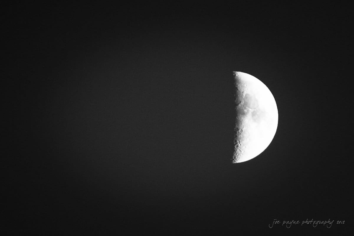 lake lure north carolina wedding photography ~ shannon and paul A black and white image of the moon in its first quarter phase. The left half is in shadow, while the right half is illuminated, showcasing detailed craters and surface texture against a dark sky.