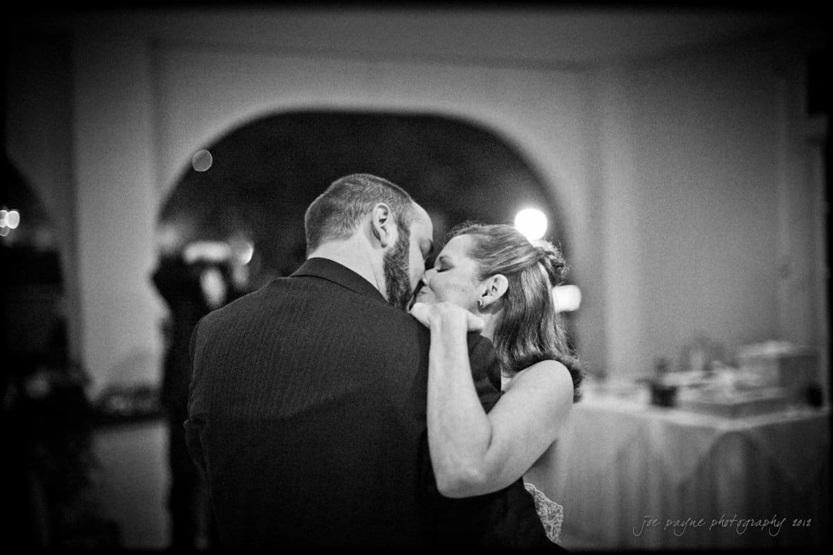 lake lure north carolina wedding photography ~ shannon and paul A couple shares a tender moment while dancing, holding each other close. The setting appears to be a dimly lit reception area, with tables and decorations visible in the background. Their expressions convey intimacy and joy.