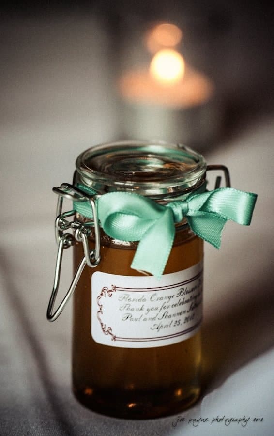 lake lure north carolina wedding photography ~ shannon and paul A small jar filled with amber liquid, adorned with a green ribbon and a label. A lit candle can be seen blurred in the background.