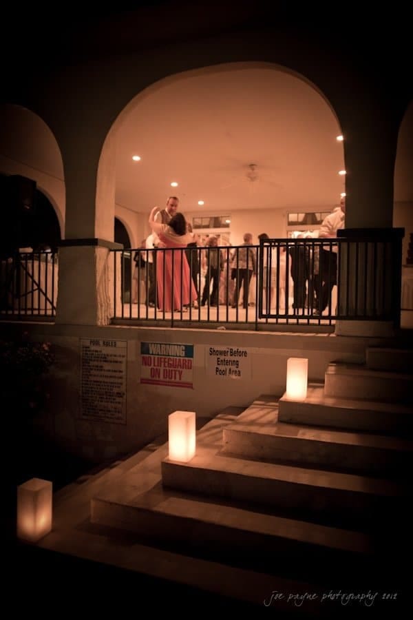 lake lure north carolina wedding photography ~ shannon and paul A couple dances on a brightly lit balcony during a nighttime event. Soft glowing lights line the steps leading up to the covered area, where guests can be seen in the background. Signs on the wall indicate pool safety instructions.