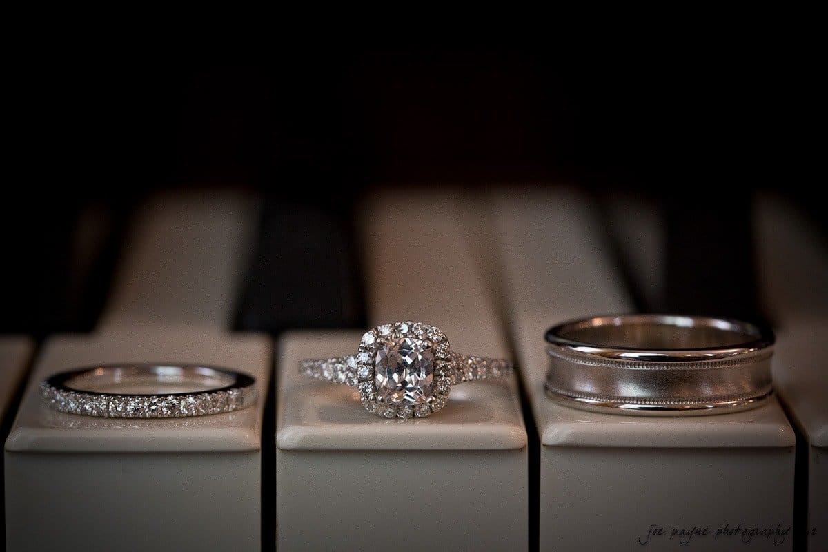carolina inn wedding photography ~ danielle and thomas Three rings are displayed on piano keys: a thin band with small diamonds, a central ring with a large oval diamond surrounded by smaller diamonds, and a wide metallic band with a smooth finish.