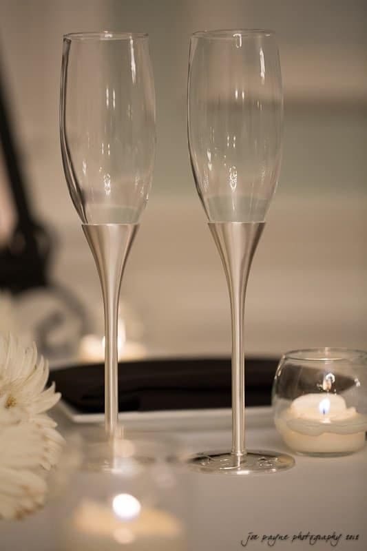 carolina inn wedding photography ~ danielle and thomas Two elegant champagne flutes with silver stems are placed on a table. Around them, a lit tealight candle and white daisy create a romantic ambiance.