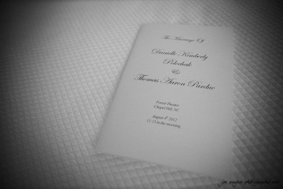 carolina inn wedding photography ~ danielle and thomas A wedding program with elegant script text lies on a textured white surface. The program details a ceremony for Danielle Kimberly Pietschak and Thomas Aaron Pardue at Forest Theatre, Chapel Hill, NC, on August 4, 2012, at 11:15 a.m.