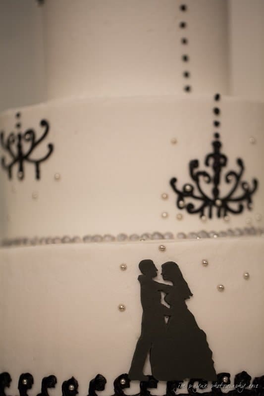 carolina inn wedding photography ~ danielle and thomas A white wedding cake with three tiers, decorated with black silhouettes of a couple dancing, intricate chandelier designs, and small pearl-like embellishments.