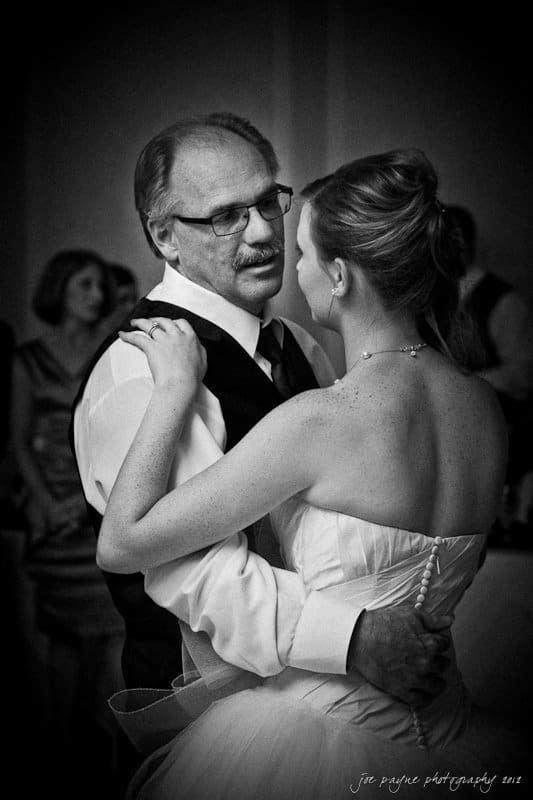 carolina inn wedding photography ~ danielle and thomas A black and white photo of a bride and an older man dancing at a wedding. The woman is in a white gown, and the man is wearing glasses and a vest. They gaze at each other in a tender moment. Others are blurred in the background.