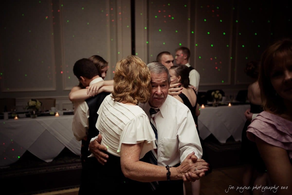 carolina inn wedding photography ~ danielle and thomas A couple dances closely on a dimly lit dance floor, surrounded by other couples. The man wears a white shirt and tie, while the woman wears a white blouse. Soft lighting creates a warm, intimate atmosphere at the event.