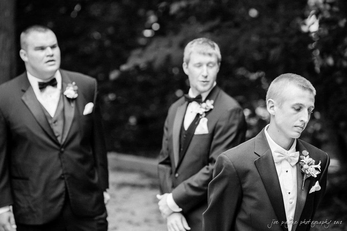 carolina inn wedding photography ~ danielle and thomas Black and white image of three men in suits and bow ties, standing outdoors. Each man has a boutonniere on their lapel. The background is blurred, focusing on the men.