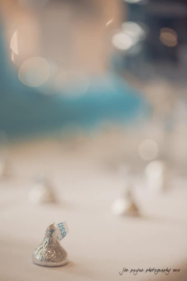 Close-up of several foil-wrapped chocolate kisses on a blurred table, with one prominently in focus. The soft background includes a hint of blue, adding a dreamy atmosphere to the scene.