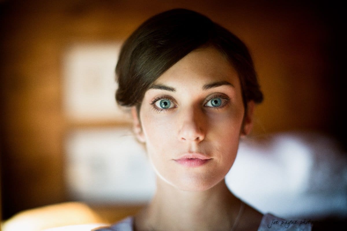 barn at valhalla, chapel hill wedding photography ~ allegra and chris Portrait of a woman with short brown hair, gazing directly at the camera. The background is softly blurred, emphasizing her facial features and expression. The lighting casts a soft glow on her face, contributing to a serene atmosphere.