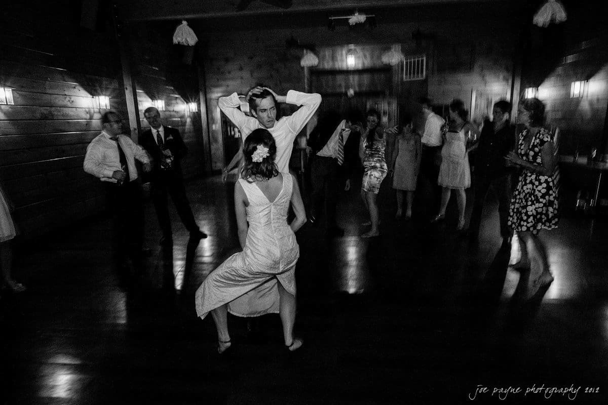 barn at valhalla, chapel hill wedding photography ~ allegra and chris A black and white photo of a lively dance floor. A couple is dancing energetically in the center, surrounded by guests. The woman wears a dress with a flower in her hair, while the man is dressed in a suit.