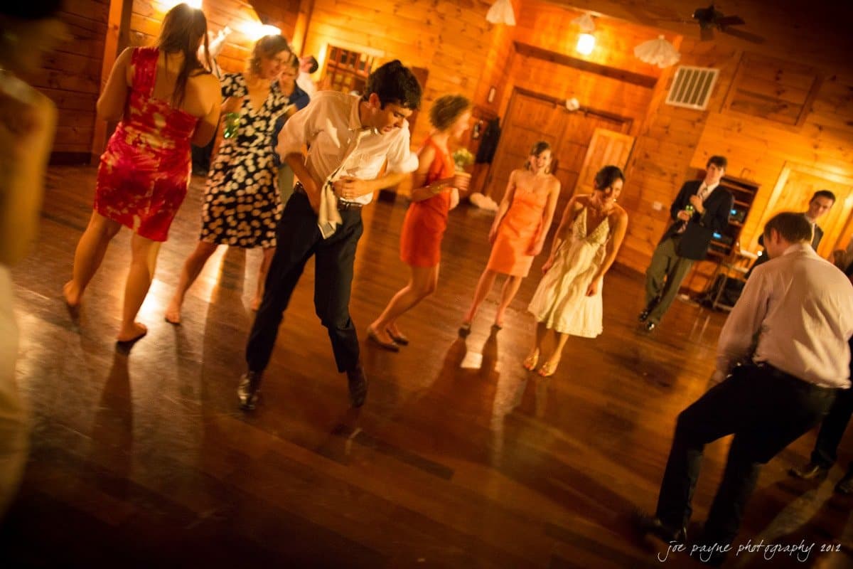 barn at valhalla, chapel hill wedding photography ~ allegra and chris A group of people dancing in a warmly lit wooden-floored room. They appear to be enjoying a lively gathering or celebration, with some wearing formal attire. The atmosphere is energetic and joyful.