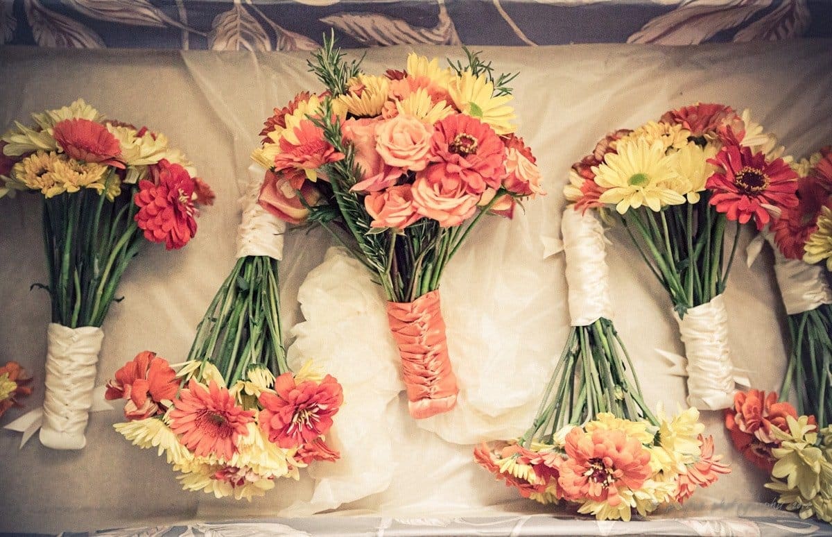 A display of colorful bouquets with orange, yellow, and red flowers, wrapped with white and orange ribbons, arranged neatly on a light background.